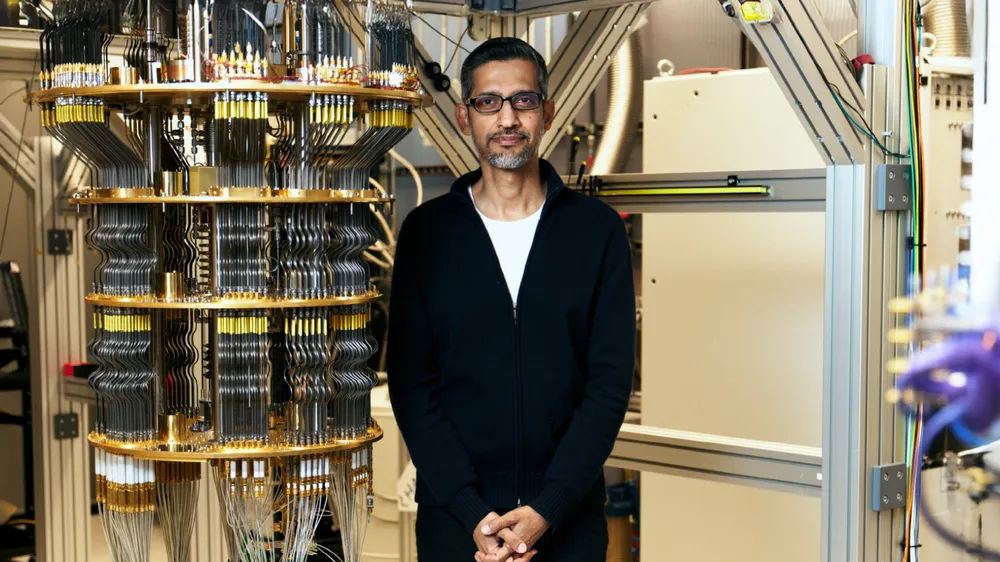 Google CEO Sundar Pichai standing beside the dilution refrigerator housing the Willow quantum processor, showing the full cryogenic system scale
